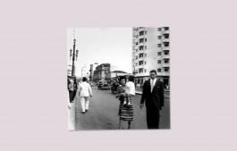 Urban scene in São Paolo, woman crossing the road in a striped dress holding a child and a man in a black suit with a white shirt and tie. Elizabeth Kutesko